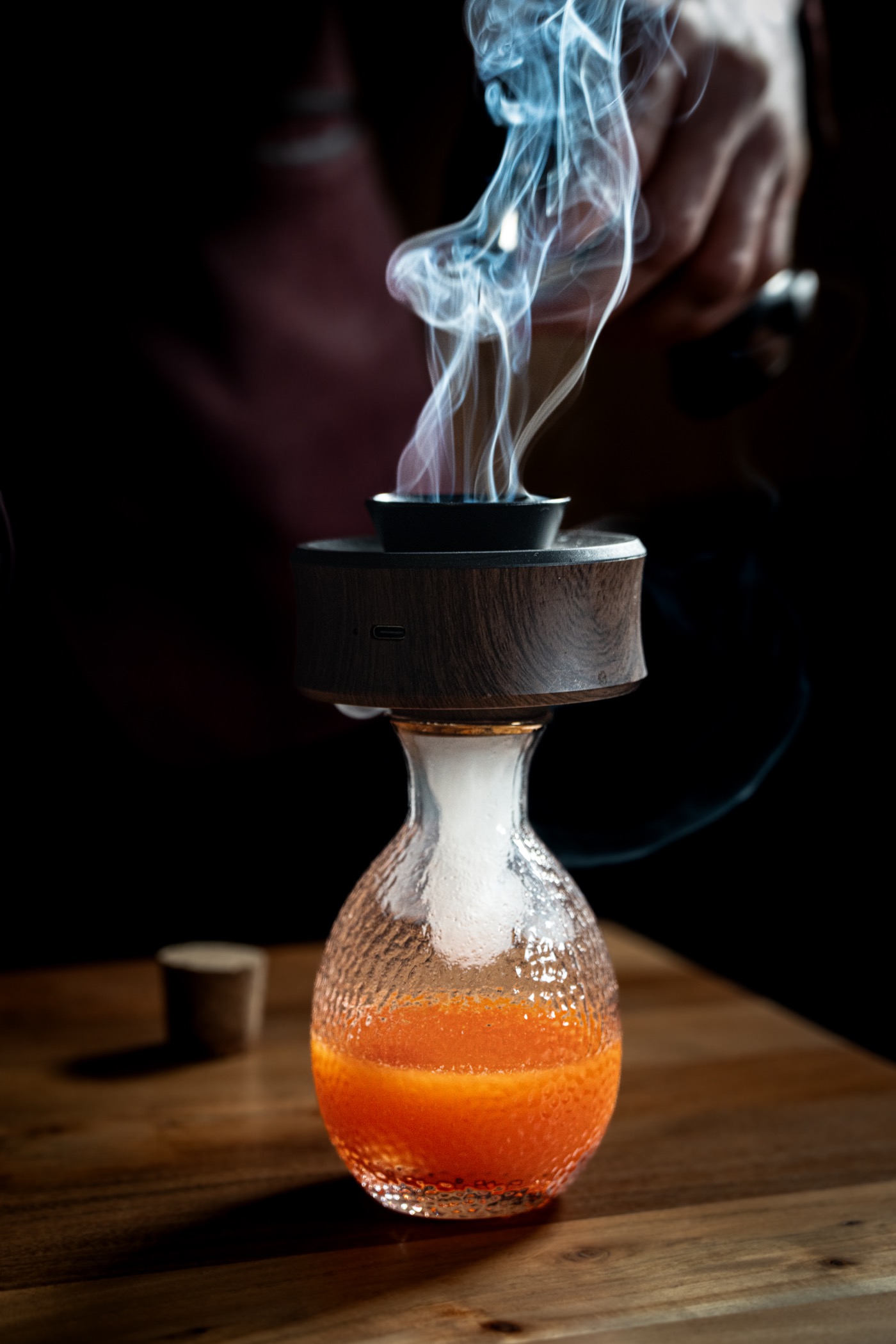 Smoke rising from a glass decanter under a wooden smoking lid