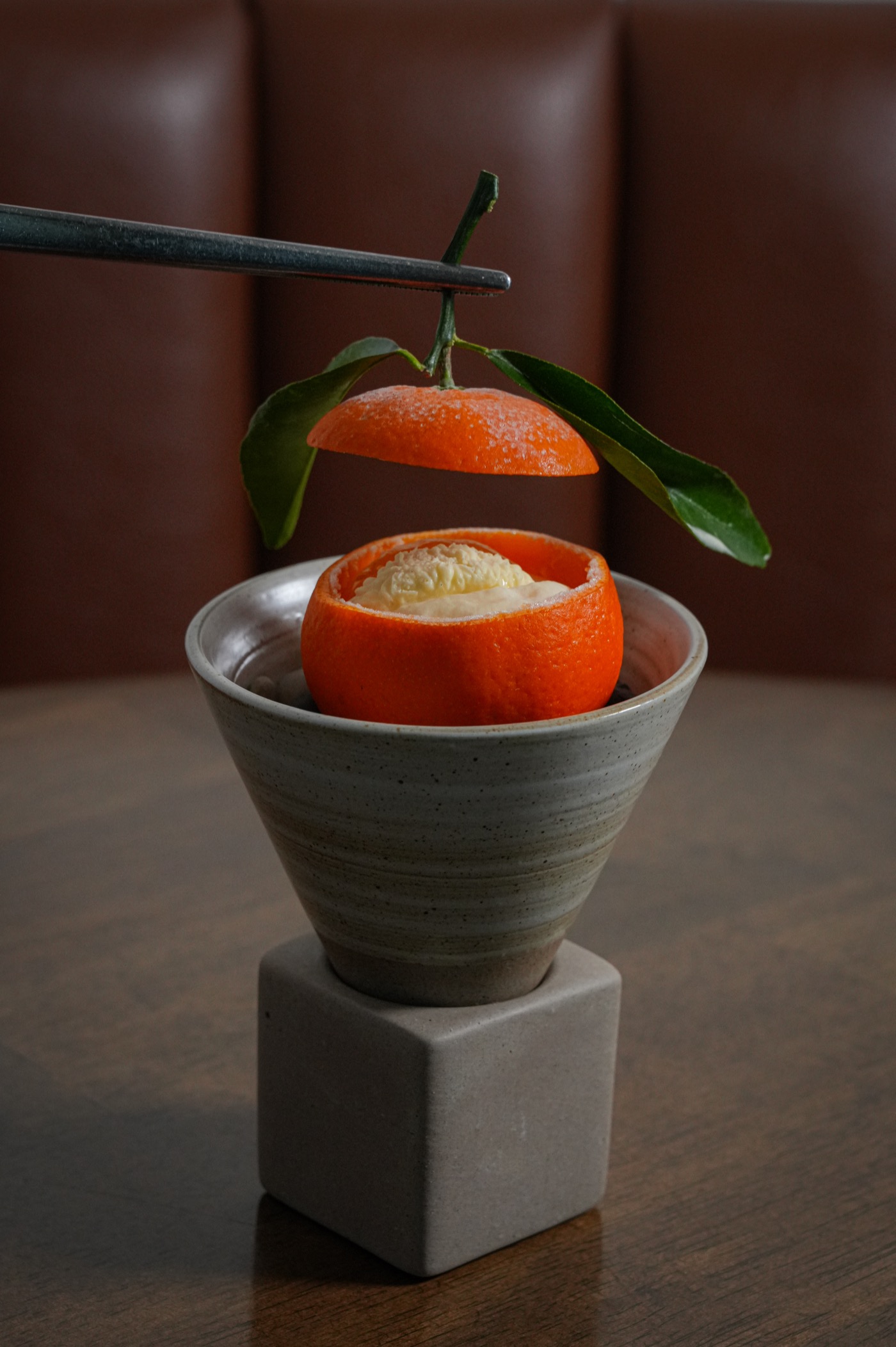 Tweezers lifting the cap from a mandarin filled with cream, plated on a ceramic stand
