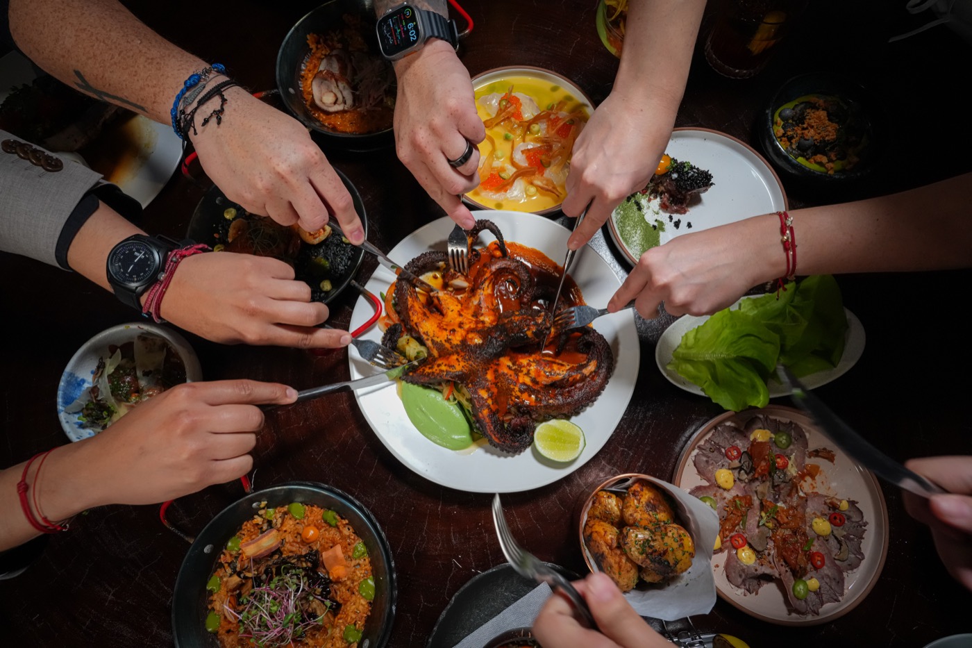 Many hands reaching across a shared table of dishes, seen from above