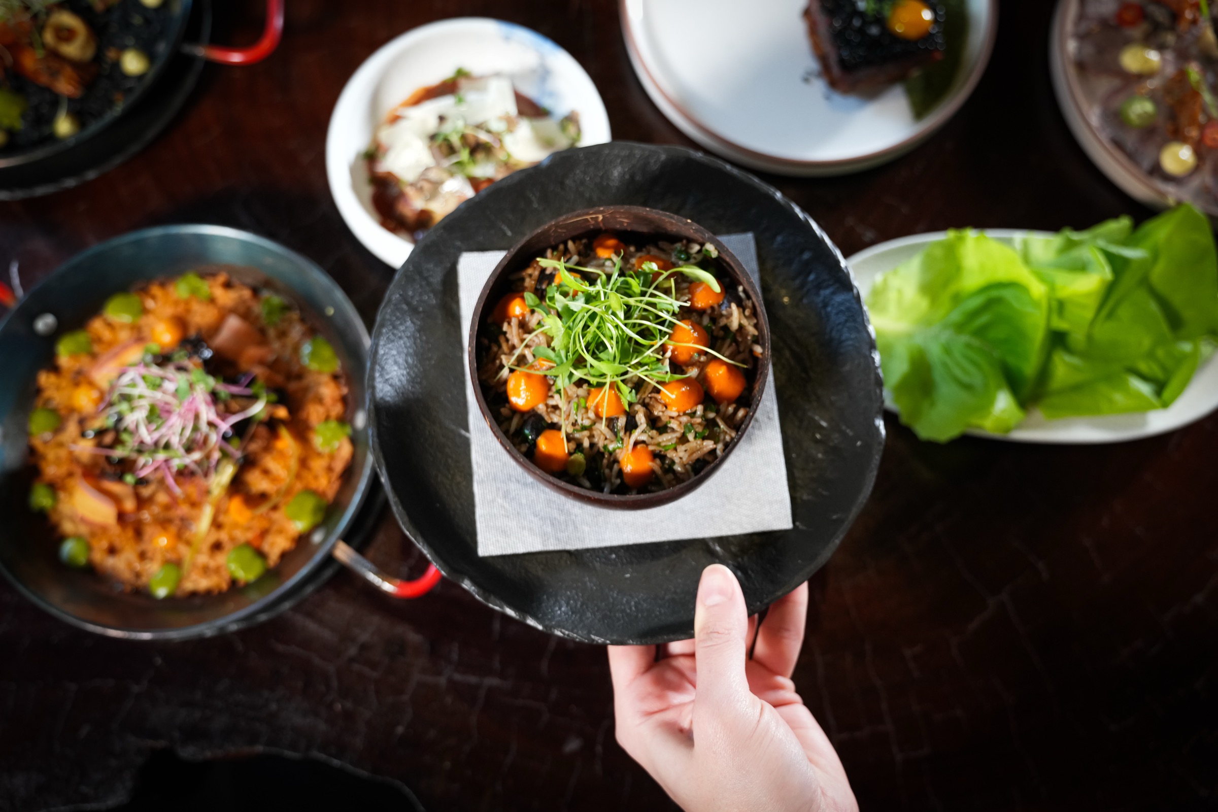 A chef's hand presenting a plated dish above a table of finished plates